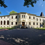 Altes-Kurhaus-Panorama.jpg Altes Kurhaus mit großen Fenstern, umgeben von Bäumen, in Bad Zwischenahn unter blauem Himmel.