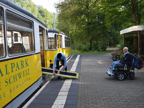 Kirnitzschtalbahn - bezbariérová lanovka Ein Schaffner legt eine Rollstuhlrampe an die Kirnitzschtalbahn an A conductor attaches a wheelchair ramp to the Kirnitzschtalbahn Průvodčí připevňuje k železnici rampu pro Kirnitzschtalbahn .Een conducteur bevestigt een rolstoelhelling aan Kirnitzschtalbahn