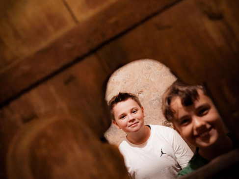 Zwei Jungen blicken durch eine rustikale Holzstruktur und lachen in die Kamera.