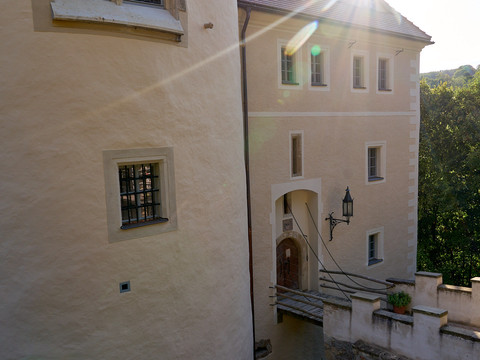 Sonnendurchflutete Fassade des Schlosses mit Fenstern und Eingangstür.Sunlit façade of the castle with windows and entrance door.Prosluněné průčelí hradu s okny a vstupními dveřmi.Oświetlona słońcem fasada zamku z oknami i drzwiami wejściowymi.Zonovergoten voorgevel van het kasteel met ramen en toegangsdeur.Facciata illuminata dal sole del castello con finestre e porta d'ingresso.