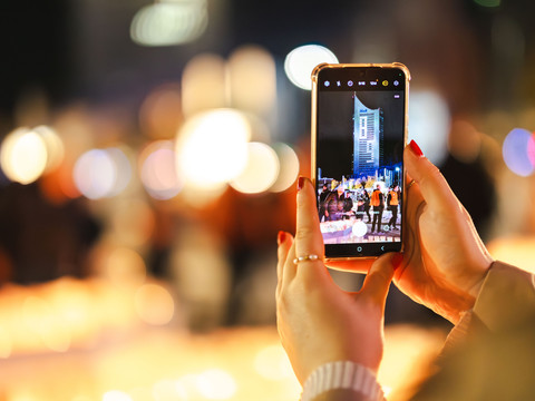 Osoba trzymająca smartfon pokazujący nocny krajobraz miasta z oświetlonym budynkiem.