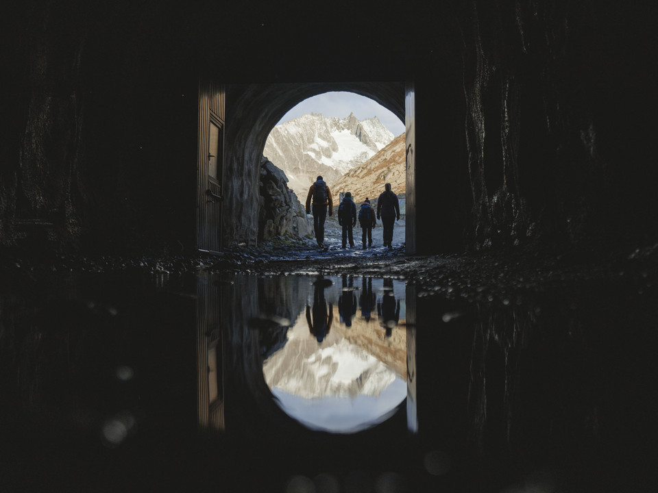 Exit through the Tälligrat Tunnel Teilnehmer der Aletschgletscher Rundtour verlassen den Tälligrattunnel mit Blick auf verschneite Berge und FelsenParticipants on the Aletsch Glacier round tour leave the Tälligrat Tunnel with a view of snow-covered mountains and rocksLes participants au circuit du glacier d'Aletsch quittent le tunnel du Tälligrat avec vue sur les montagnes et les rochers enneigés.