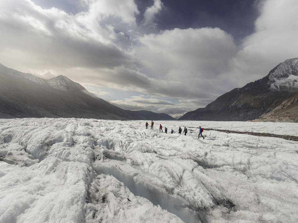 Wandergruppe auf dem Eisfeld Gruppe während der Aletschgletscher Rundtour bewegt sich über weite Eisflächen mit dramatischem Himmel im HintergrundGroup during the Aletsch Glacier round trip moving over wide ice surfaces with dramatic sky in the backgroundLe groupe pendant le tour du glacier d'Aletsch se déplace sur de vastes étendues de glace avec un ciel dramatique en arrière-plan.