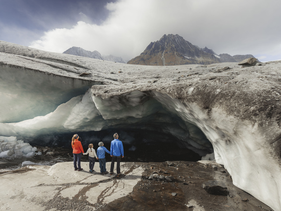 Family discovers ice cave on the Aletsch Glacier Familie steht vor einer Eishöhle am Aletschgletscher während der Gletschertour Jungfraujoch MärjelenseeFamily standing in front of an ice cave on the Aletsch Glacier during the Jungfraujoch Märjelensee glacier tourFamille devant une grotte de glace sur le glacier d'Aletsch pendant le tour du glacier Jungfraujoch Märjelensee