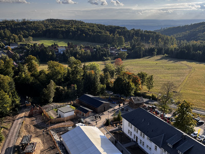 Grüne Landschaft unter blauem Himmel, teils bewaldet, mit vereinzelten Gebäuden und Wegen als Ausblick vom HEX Aussichtsturm.