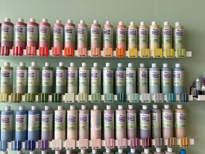 Lieblingstasse-Farben.jpg Farbflaschen nach Farben geordnet in Reihe an einer Wand