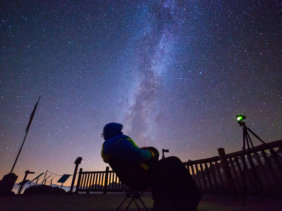 Starry sky above the observation deck Sternenfotografie Bettmerhorn mit Beobachter im Stuhl unter der Milchstrasse über den verschneiten Bergen der Aletsch ArenaStar photography Bettmerhorn with observer in chair under the Milky Way above the snow-covered mountains of the Aletsch ArenaPhotographie d'étoiles Bettmerhorn avec un observateur dans une chaise sous la voie lactée au-dessus des montagnes enneigées de l'Aletsch Arena