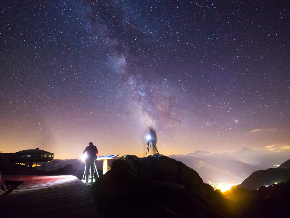 Milky Way above the mountain silhouette Sternenfotografie Bettmerhorn mit leuchtender Milchstrasse über den Walliser Alpen und zwei Fotografen im VordergrundStar photography Bettmerhorn with glowing Milky Way over the Valais Alps and two photographers in the foregroundPhotographie étoilée du Bettmerhorn avec une voie lactée lumineuse au-dessus des Alpes valaisannes et deux photographes au premier plan