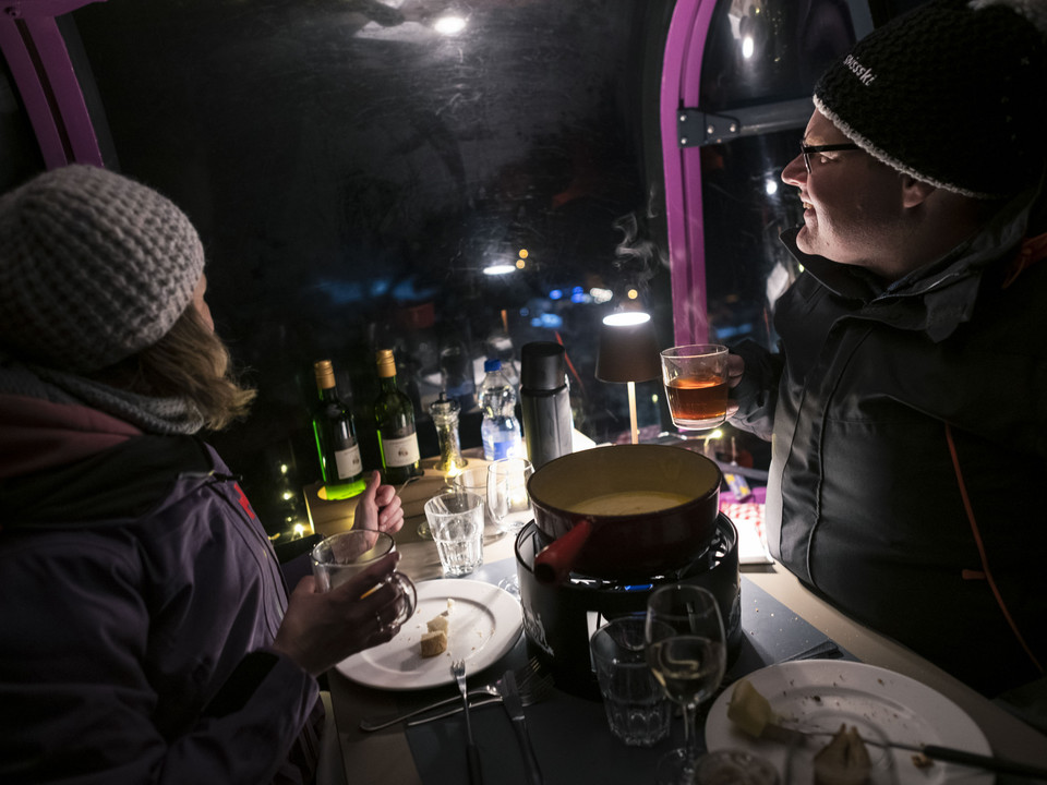 Fondue evening with wine in the gondola Fonduegondel Bettmerhorn mit Paar, das Wein und Käsefondue bei stimmungsvoller Beleuchtung in der Gondelbahn geniesstBettmerhorn fondue gondola with couple enjoying wine and cheese fondue under atmospheric lighting in the gondola liftTélécabine pour fondue Bettmerhorn avec un couple dégustant du vin et une fondue au fromage sous un éclairage d'ambiance dans la télécabine