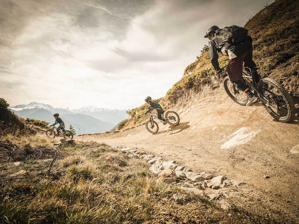 Expérience de flowtrail en famille Passeport VTT haut-valaisan avec des vététistes sur le flowtrail Wurzenbord au-dessus de Bettmeralp dans l'Aletsch Arena avec panorama sur les Alpes