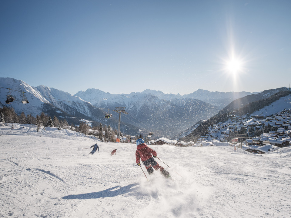 Skiing in the sunshine in the Aletsch Arena Skipass Aletsch Arena mit Skifahrern bei sonnigem Wetter auf der Piste oberhalb der Bettmeralp mit Blick auf verschneite ChaletsAletsch Arena ski pass with skiers in sunny weather on the piste above Bettmeralp with a view of snow-covered chaletsForfait Aletsch Arena avec skieurs par temps ensoleillé sur la piste au-dessus de Bettmeralp avec vue sur les chalets enneigés