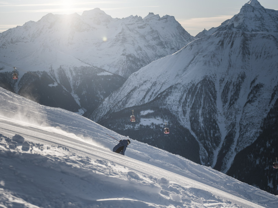 Erste Spuren im frischen Schnee Skipass Aletsch Arena mit Skifahrer bei Sonnenaufgang auf dem Bettmerhorn, während die Gondeln über verschneite Berghänge gleitenAletsch Arena ski pass with skiers at sunrise on the Bettmerhorn, while the gondolas glide over snow-covered mountain slopesForfait Aletsch Arena avec skieurs au lever du soleil sur le Bettmerhorn, tandis que les télécabines glissent sur les versants enneigés de la montagne