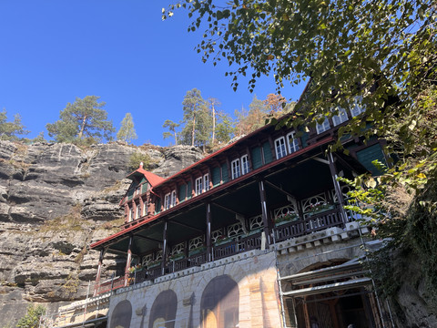 Vordergrund Gaststätte im Schweizer Baustil und im Hintergrund Sandsteinfelsen.