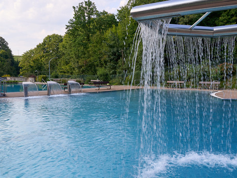 Schwimmbad mit Wasserfall und umgebender Grünanlage.