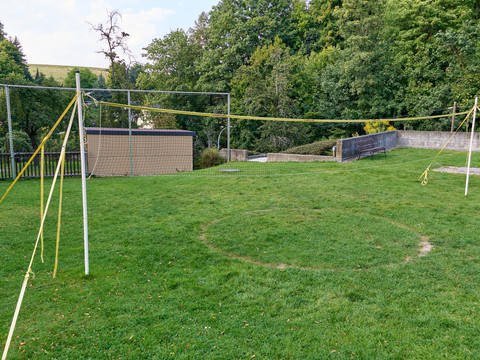 Stadtbad Hohnstein Leerer Volleyballplatz auf grüner Wiese mit Netz und Metallzaun im Hintergrund.