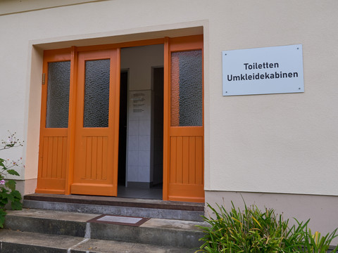 Stadtbad Hohnstein Orangefarbene Türen eines Gebäudes mit Schild "Toiletten Umkleidekabinen" an der Wand.