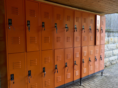 Stadtbad Hohnstein Reihe orangefarbener Schließfächer mit Vorhängeschlössern unter einem Überdach.