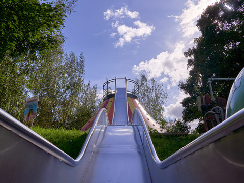 Metallrutsche im Freien mit Blick auf Bäume und blauen Himmel mit Wolken.