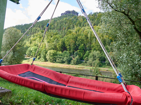 Rote Hängematte mit Blick auf bewaldeten Hügel mit Lilienstein und Elbe.