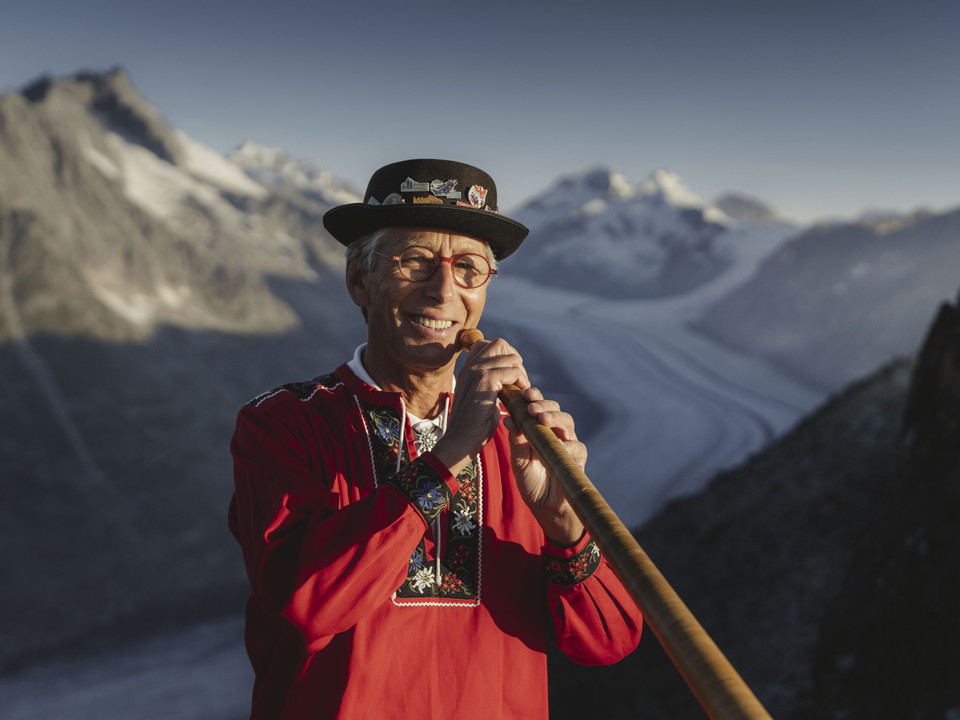 Les sons du cor des Alpes au-dessus du glacier d'Aletsch Sonnenaufgangsfahrt Eggishorn mit Alphornbläser in traditioneller Tracht vor dem Aletschgletscher und den Walliser AlpenSunrise tour Eggishorn with alphorn players in traditional costume in front of the Aletsch Glacier and the Valais AlpsExcursion au lever du soleil à Eggishorn avec un joueur de cor des Alpes en costume traditionnel devant le glacier d'Aletsch et les Alpes valaisannes