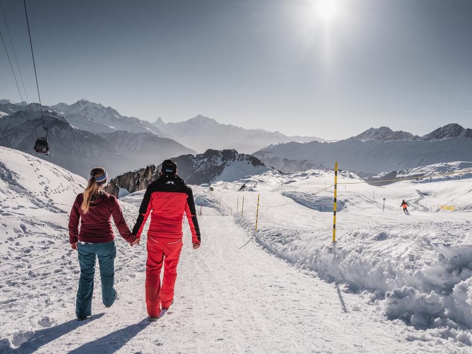 Gemeinsam durch den Winter Aletsch Entdeckerpass mit Paar beim Winterwandern in der verschneiten Aletsch Arena mit Sonnenschein