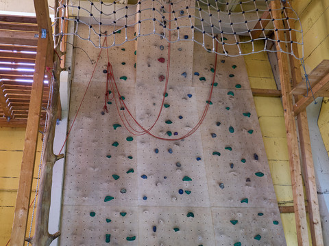 Kletterwand mit bunten Griffen und Netz in einer Indoor-Kletterhalle.