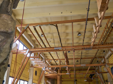 Blick auf die Deckenkonstruktion einer Kletterhalle mit Holzbalken und Kletterelementen.