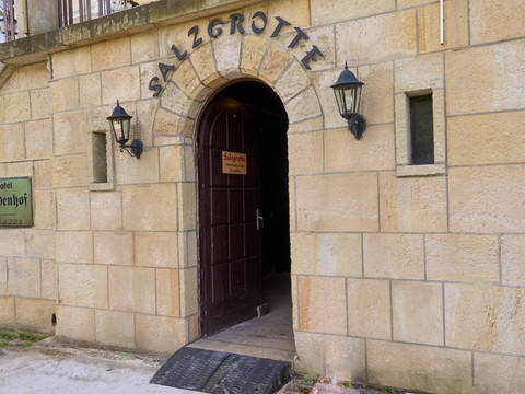 Steinportal mit Holztür, darüber Schriftzug "Salzgrotte", zwei Wandlampen.Stone portal with wooden door, "Salzgrotte" lettering above, two wall lamps.Kamenný portál s dřevěnými dveřmi, nad nimi nápis "Salzgrotte", dvě nástěnné lampy.Kamienny portal z drewnianymi drzwiami, napis "Salzgrotte" powyżej, dwie lampy ścienne.Stenen portaal met houten deur, "Salzgrotte" opschrift erboven, twee wandlampen.Portale in pietra con porta in legno, scritta "Salzgrotte" in alto, due lampade a muro.
