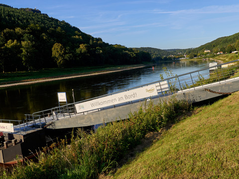 Elbe mit Anlegestelle und Schild "Willkommen an Bord", bewaldete Hügel im Hintergrund.Elbe with landing stage and "Welcome aboard" sign, wooded hills in the background.Labe s přistávacím můstkem a nápisem "Vítejte na palubě", v pozadí zalesněné kopce.Łaba z lądowiskiem i napisem "Witamy na pokładzie", w tle zalesione wzgórza.Elbe met aanlegsteiger en bord "Welkom aan boord", beboste heuvels op de achtergrond.Elba con pontile e cartello "Benvenuti a bordo", sullo sfondo colline boscose.