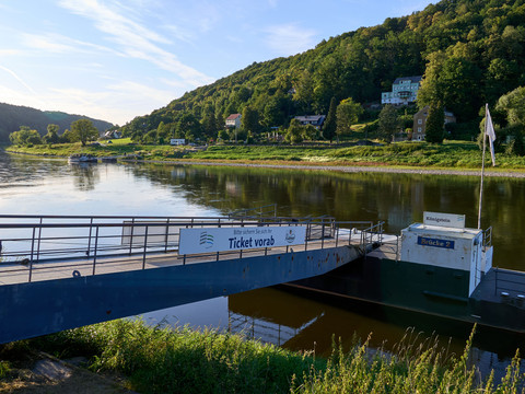 Dampfschiff Anlegestelle Königstein  Elbe mit Anlegestelle und Schild "Ticketverkauf", bewaldete Hügel im Hintergrund.
