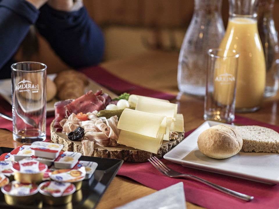 Frühstück mit Walliser Spezialitäten First Track Bettmerhorn mit Käseplatte, Aufschnitt, Brot und Orangensaft auf rustikalem HolztischFirst Track Bettmerhorn with cheese platter, cold cuts, bread and orange juice on a rustic wooden tableFirst Track Bettmerhorn avec plateau de fromages, charcuterie, pain et jus d'orange sur une table rustique en bois