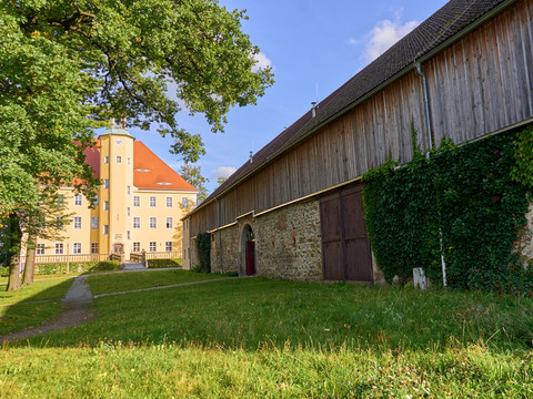 Kuturscheune Große Scheune aus Stein und Holz neben gelbem Gebäude, umgeben von Bäumen und Gras.Large barn made of stone and wood next to a yellow building, surrounded by trees and grass.Velká stodola z kamene a dřeva vedle žluté budovy, obklopená stromy a trávou.Duża stodoła z kamienia i drewna obok żółtego budynku, otoczona drzewami i trawą.Grote schuur van steen en hout naast een geel gebouw, omringd door bomen en gras.Grande fienile in pietra e legno accanto a un edificio giallo, circondato da alberi ed erba.