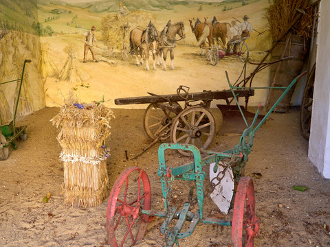 Alte landwirtschaftliche Geräte und Wagen in einer Scheune mit Wandgemälde.Old agricultural equipment and carts in a barn with murals.Stará zemědělská technika a vozy ve stodole s nástěnnými malbami.Stary sprzęt rolniczy i wozy w stodole z malowidłami ściennymi.Oude landbouwmachines en karren in een schuur met muurschilderingen.Vecchie attrezzature agricole e carri in un fienile con murales.