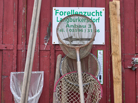 Forellen und Lachszucht Ermisch Fischernetze an roter Holzwand mit Schild "Forellanzucht Langburkersdorf Anbau 3".Fishing nets on red wooden wall with sign "Forellanzucht Langburkersdorf Anbau 3".Rybářské sítě na červené dřevěné stěně s nápisem "Forellanzucht Langburkersdorf Anbau 3".Sieci rybackie na czerwonej drewnianej ścianie z napisem "Forellanzucht Langburkersdorf Anbau 3".Visnetten op rode houten muur met bord "Forellanzucht Langburkersdorf Anbau 3".Reti da pesca su una parete di legno rosso con l'insegna "Forellanzucht Langburkersdorf Anbau 3".