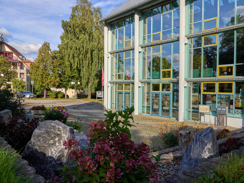Neustadthalle Glasfassade eines modernen Gebäudes mit umgebender Gartenlandschaft und Bäumen.