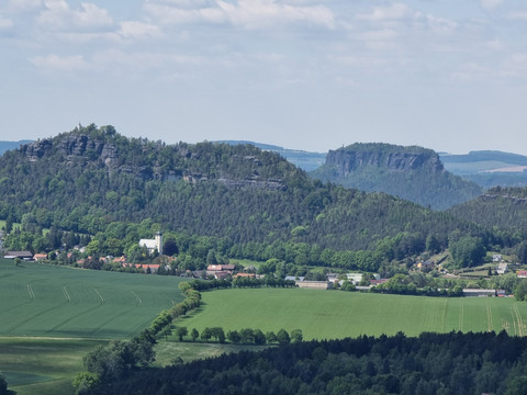 Blick vom Kleinen Zschirnstein Bewaldete Hügel mit Felsen und einer kleinen Ortschaft im Tal.
