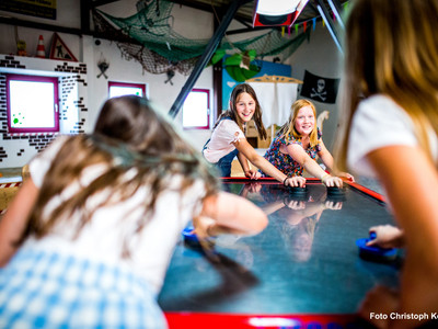 Kinder spielen fröhlich Airhockey in der bunten Happylino Indoor-Spielhalle mit Piratendekoration.
