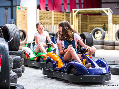 Zwei Kinder fahren lachend mit bunten E-Karts durch die Happylino Indoor-Bahn aus aufgestapelten Reifen.