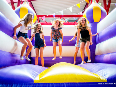 Kinder springen lachend auf einer lila-gelben Hüpfburg in der Happylino Halle.