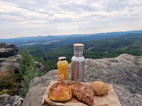 Picknick auf einem Felsen mit Ausblick auf bewaldete Hügel, inklusive Gebäck und Getränke.