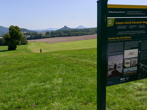 Caspar David Friedrich Informationsstele im Vordergrund, Landschaft mit Feldern und Hügeln im Hintergrund.