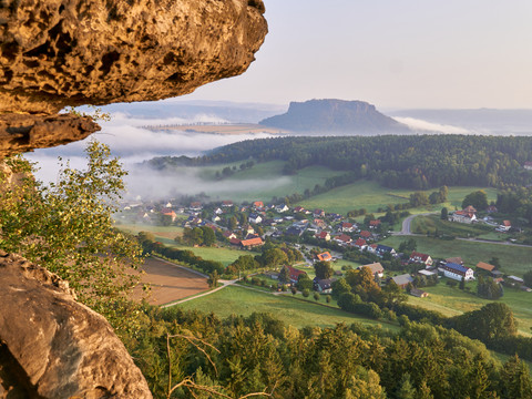 Lilienstein über Nebelmeer, umgeben von Wald und Feldern im Morgenlicht.