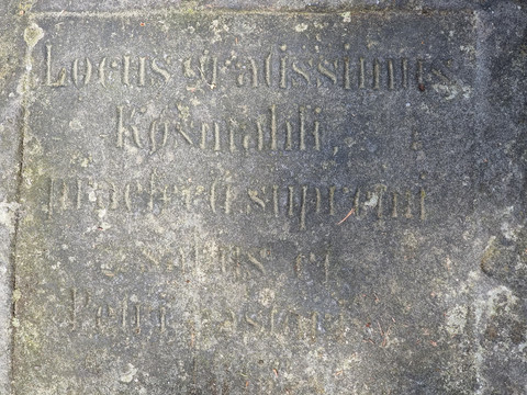 Verwitterte Steintafel mit eingravierten lateinischen Buchstaben, teilweise unleserlich.