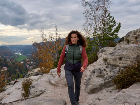 Frau wandert auf felsigem Bergpfad mit bewölktem Himmel im Hintergrund.