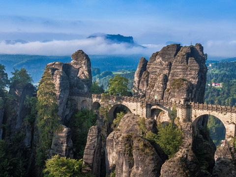 Bastei Brücke Felsformationen mit Brücke und Nebel über bewaldeten Bergen im Hintergrund.Rock formations with bridge and fog over forested mountains in the background.Skalní útvary s mostem a mlhou nad zalesněnými horami v pozadí.Formacje skalne z mostem i mgłą nad zalesionymi górami w tle.Rotsformaties met brug en mist boven beboste bergen op de achtergrond.Formazioni rocciose con ponte e nebbia su montagne boscose sullo sfondo.