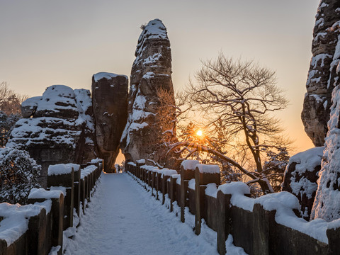Schneebedeckter Weg zwischen Felsformationen bei Sonnenuntergang.