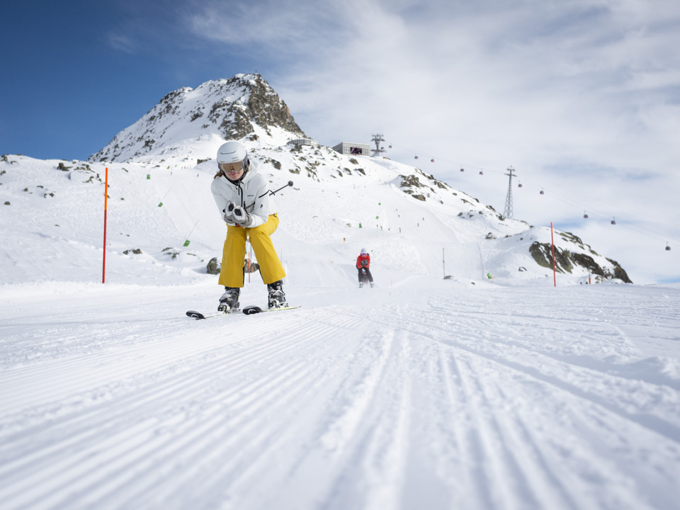 Skier on the descent in the Aletsch Arena Beim Wahltages Skipass Aletsch Arena fährt eine Skifahrerin in gelber Hose konzentriert die frisch präparierte Piste hinunter unter blauem HimmelOn the Aletsch Arena ski pass election day, a skier in yellow pants skis down the freshly groomed slope under a blue skyLors de la journée de choix du forfait de ski Aletsch Arena, une skieuse en pantalon jaune dévale avec concentration la piste fraîchement préparée sous un ciel bleu.