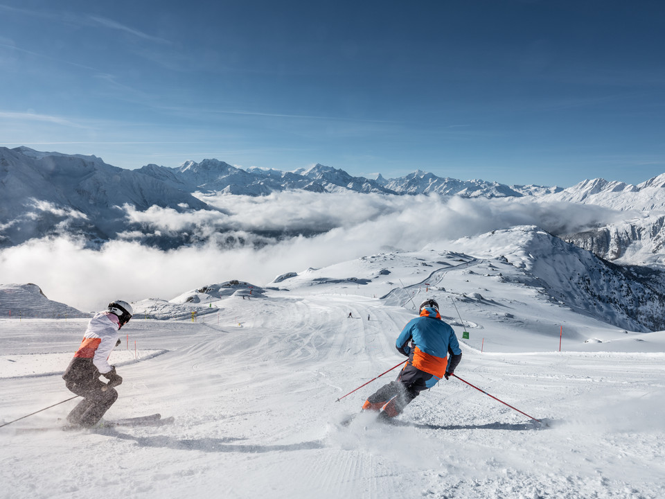 Dynamisches Skifahren mit Blick auf die Walliser Alpen Beim Wahltages Skipass Aletsch Arena fahren zwei Skifahrer in eleganten Schwüngen über die breite Panoramapiste mit Blick auf die Walliser AlpenWith the optional Aletsch Arena ski pass, two skiers make elegant turns on the wide panoramic slope with views of the Valais AlpsAvec le forfait à choix Aletsch Arena, deux skieurs effectuent des virages élégants sur la large piste panoramique avec vue sur les Alpes valaisannes.