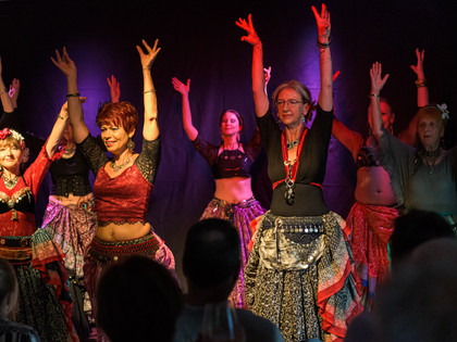 Kulturnacht Wolfenbüttel 2023,DSC_4130.jpg Tanzgruppe in bunten Kleidern hebt die Arme bei bunter Beleuchtung.