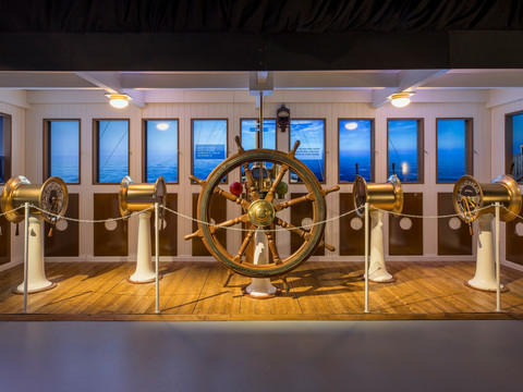 Nachbildung der Steuerbrücke mit Steuerrad und Geschwindigkeitsregler in der Ausstellung "Titanic: Eine Immersive Reise"Replica of the steering bridge with steering wheel and cruise control in the exhibition "Titanic: An Immersive Voyage"Replika kormidelního můstku s volantem a tempomatem na výstavě "Titanic: An Immersive Voyage" (Titanic: Plavba, která vás pohltí)Replika mostka sterowego z kierownicą i tempomatem na wystawie "Titanic: Wciągająca podróż"Replica van de stuurbrug met stuurwiel en cruisecontrol in de tentoonstelling "Titanic: An Immersive Voyage".Replica della plancia di comando con volante e cruise control nella mostra "Titanic: An Immersive Voyage"